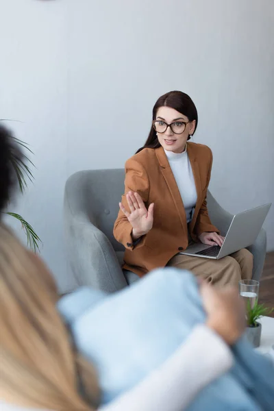 Psychologist with laptop gesturing while talking to blurred lesbian couple — Stock Photo