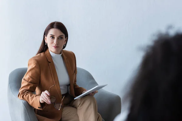 Psicologo che tiene tablet e occhiali digitali durante la consultazione con il paziente offuscato — Foto stock