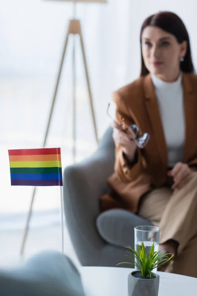 Selective focus of small lgbt flag near blurred psychologist in consulting room — Stock Photo