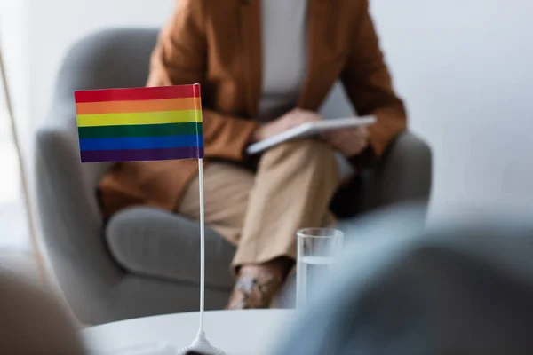 Обрезанный взгляд психолога рядом с маленьким флагом lgbt и размытые гомосексуальные пациенты — стоковое фото