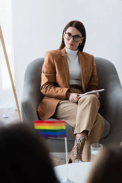 Psychologue avec tablette numérique assis près du patient et drapeau lgbt sur le premier plan flou — Photo de stock