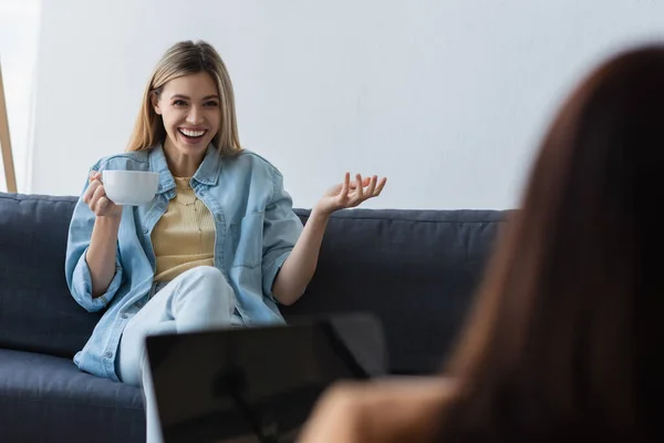 Glückliche Frau mit einer Tasse Tee im Gespräch mit Psychologen im verschwommenen Vordergrund — Stockfoto