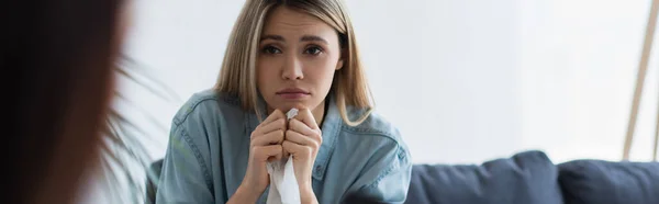 Upset woman holding paper napkin during appointment with blurred psychologist, banner — Stock Photo