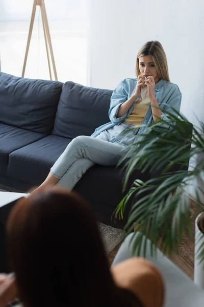 Upset woman sitting on couch during psychological consultation, blurred foreground — Stock Photo