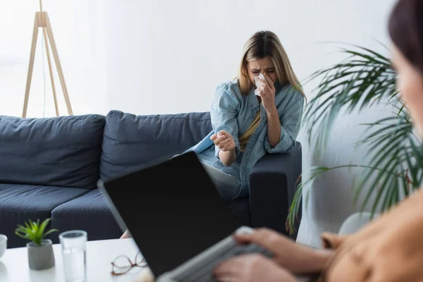 Femme déprimée pleurer sur le canapé près de psychologue floue avec ordinateur portable — Photo de stock