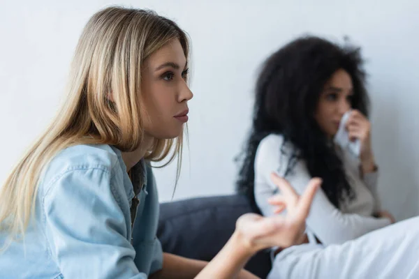 Young lesbian woman gesturing near offended african american girlfriend crying on blurred background — Stock Photo