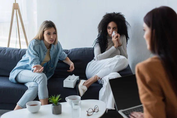 Junge lesbische Frau spricht mit verschwommenem Psychologen in der Nähe weinender afrikanisch-amerikanischer Freundin — Stockfoto