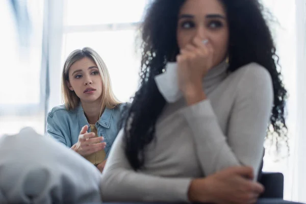 Worried lesbian woman looking at offended african american girlfriend crying on blurred foreground — Stock Photo