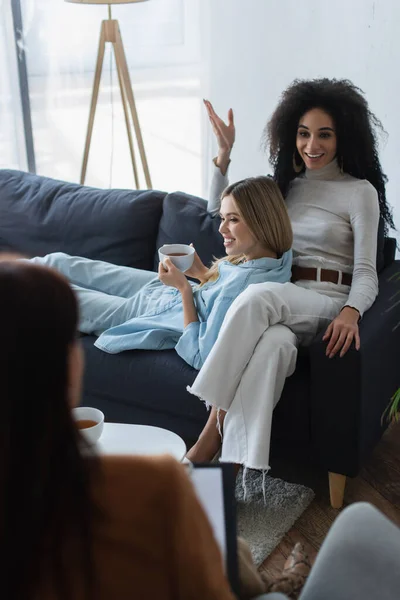 African american lesbian woman talking to blurred psychologist near girlfriend with cup of tea — Stock Photo