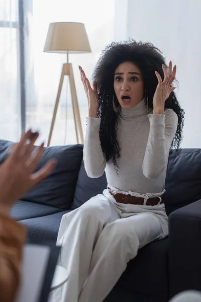 Frustrated african american woman gesturing while talking to blurred psychologist — Stock Photo