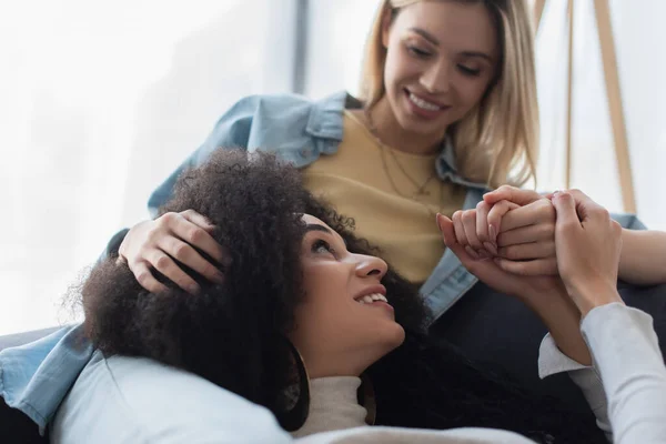 Glückliche interrassische lesbische Frauen, die sich an den Händen halten und einander anschauen — Stockfoto