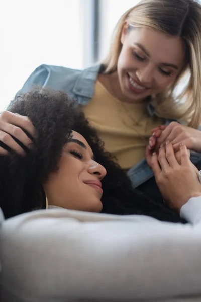 Blurred lesbian woman touching hair and holding hands of happy african american girlfriend — Stock Photo