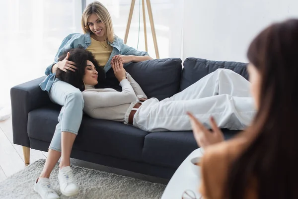 Blurred psychologist near happy interracial lesbian couple on couch in consulting room — Stock Photo