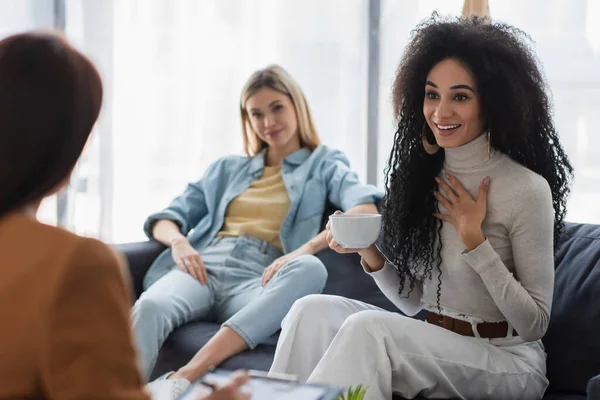 Africaine américaine femme avec tasse de thé parler à flou psychologue et lesbienne copine — Photo de stock