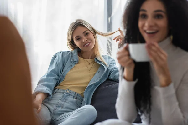 Happy lesbian woman looking at blurred african american girlfriend drinking tea during psychological consultation — Stock Photo