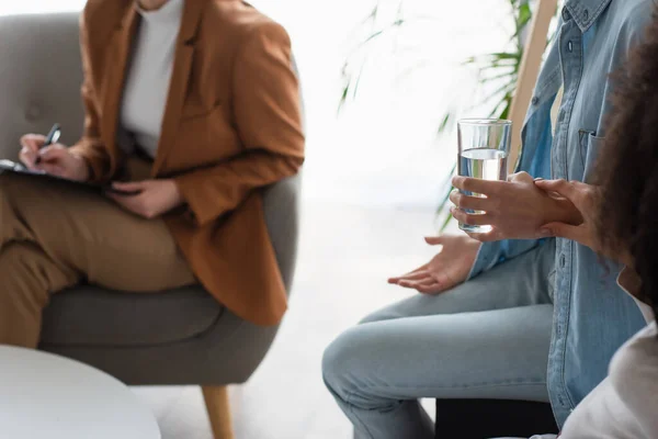 Cropped view of interracial lesbian couple near blurred psychologist in consulting room — Stock Photo