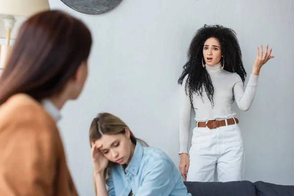 African american lesbian woman quarreling near depressed girlfriend and blurred psychologist — Stock Photo