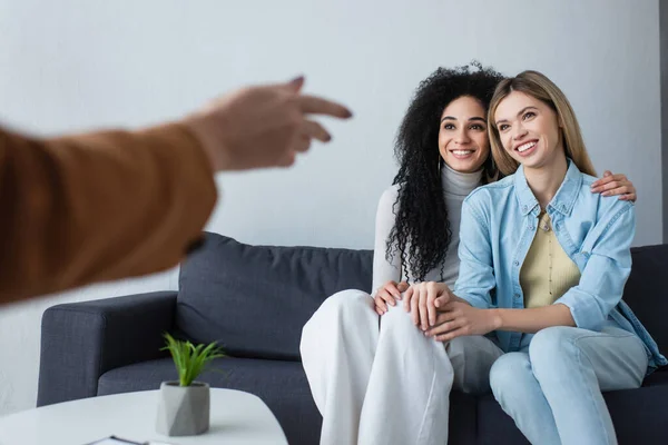 Blurred psychologist pointing at multiethnic lesbian women sitting on couch in consulting room — Stock Photo