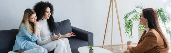 African american lesbian woman gesturing while talking to psychologist near lesbian girlfriend, banner — Stock Photo