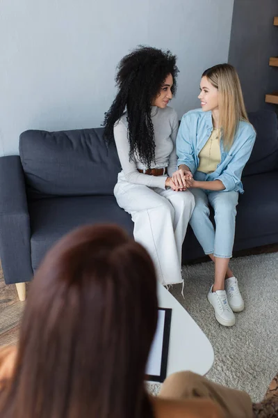 Casal interracial de lésbicas olhando umas para as outras e de mãos dadas durante a consulta psicológica — Fotografia de Stock