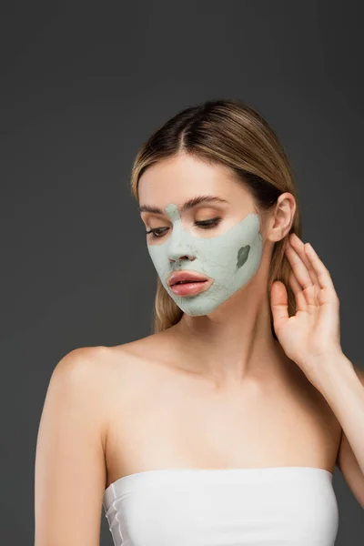Giovane donna con maschera in argilla sul viso posa isolata su grigio — Foto stock