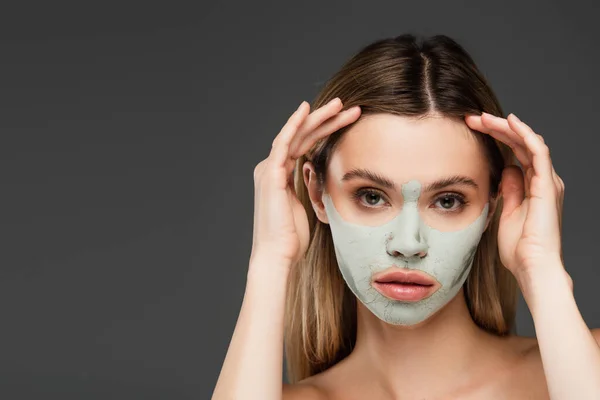 Frau mit Maske aus Ton hält die Hände vor dem Gesicht, während sie in die Kamera schaut, isoliert auf grau — Stockfoto