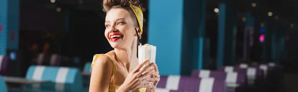 Happy pin up woman holding milkshake in glass in cafe, banner — Stock Photo