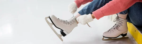 Vista cortada de mulher amarrando cadarços de sapato em patins de gelo, bandeira — Fotografia de Stock