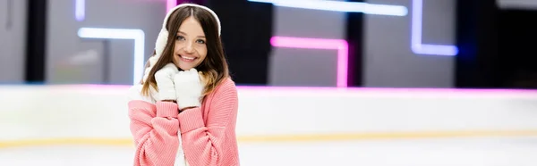 Joyful young woman in ear muffs and scarf on ice rink, banner — Stock Photo