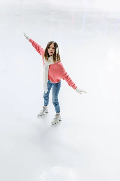 Vue grand angle de la jeune femme étonnante dans les manchons d'oreille et le patinage écharpe sur la patinoire — Photo de stock