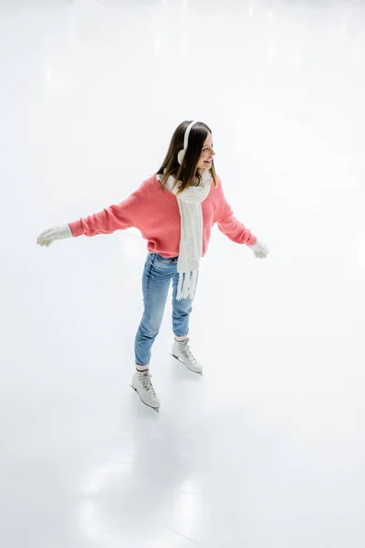 High angle view of pleased young woman in ear muffs and scarf skating on ice rink — Stock Photo