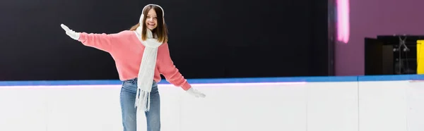 Mujer joven positiva en orejeras y bufanda en pista de hielo, pancarta - foto de stock