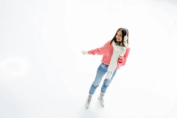 Visão de alto ângulo da jovem mulher positiva em regalos auriculares e cachecol patinação na pista de gelo — Fotografia de Stock