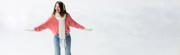 Giovane donna sorridente in paraorecchie e sciarpa sulla pista di pattinaggio, striscione — Foto stock