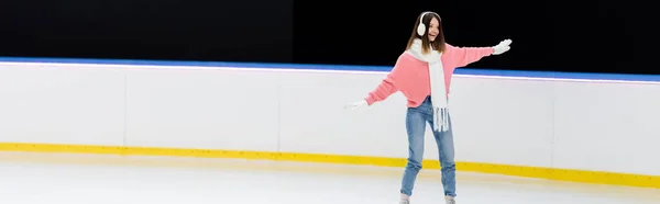 Alegre joven mujer en orejeras y bufanda patinaje en pista de hielo, pancarta - foto de stock