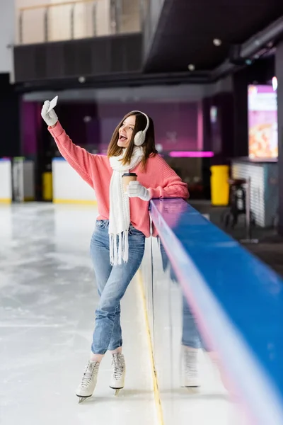 Jeune femme positive avec tasse en papier prenant selfie sur la patinoire — Photo de stock