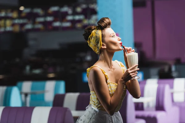 Vista lateral de pin up mulher bebendo saboroso milkshake no café — Fotografia de Stock