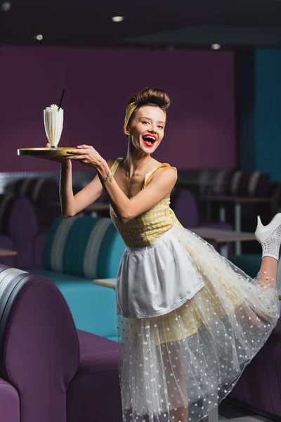 Happy pin up waitress with tattoo holding tray with milkshake in cafe — Stock Photo