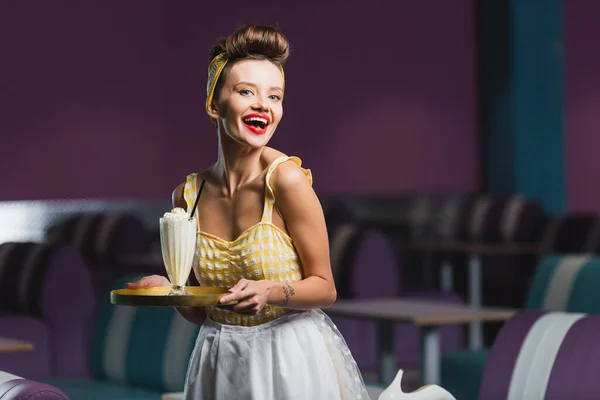 Positivo pin up camarera celebración bandeja con batido en la cafetería - foto de stock