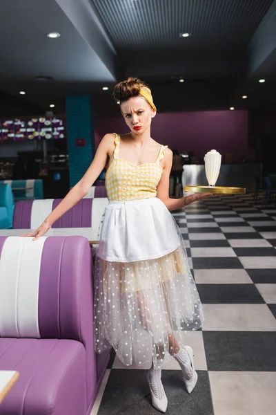 Displeased pin up waitress holding tray with milkshake in cafe — Stock Photo