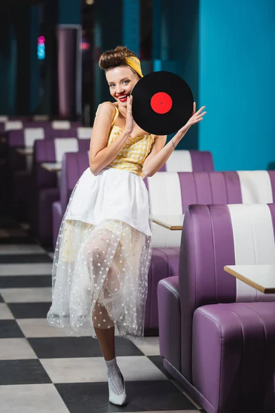 Pleine longueur de femme pin up heureux avec lèvres rouges tenant disque de vinyle rétro — Photo de stock