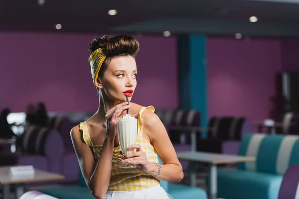 Joven pin up mujer mirando hacia otro lado mientras bebe milkshake - foto de stock