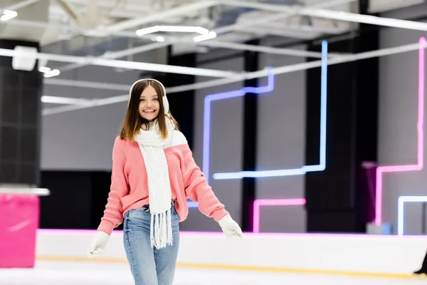 Felice donna in cuffia e maglione rosa sulla pista di pattinaggio — Foto stock