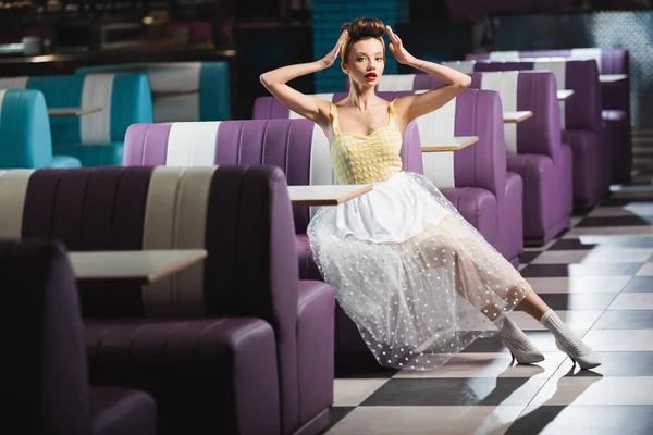 Comprimento total de jovem pin up mulher ajustando o cabelo enquanto sentado no café vintage — Fotografia de Stock