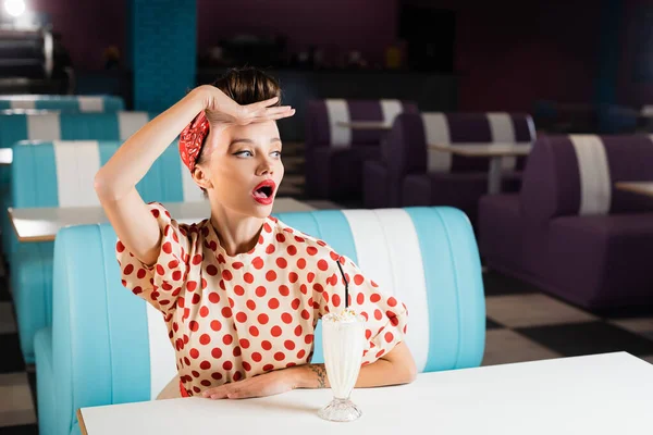 Surprise pin up femme regardant loin près milkshake sur la table — Photo de stock