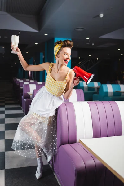 Feliz jovem pin up mulher segurando milkshake e falando em megafone — Fotografia de Stock