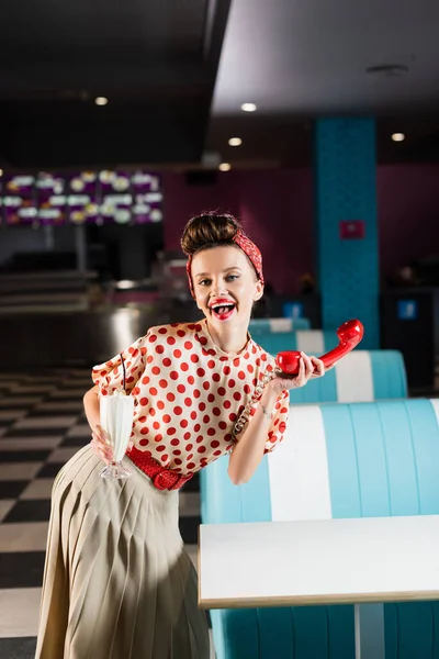 Erstaunte Pin-up-Frau mit Retro-Handy und Milchshake im Café — Stockfoto