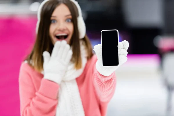 Расплывчатая и изумленная женщина в перчатках держит смартфон с пустым экраном — стоковое фото