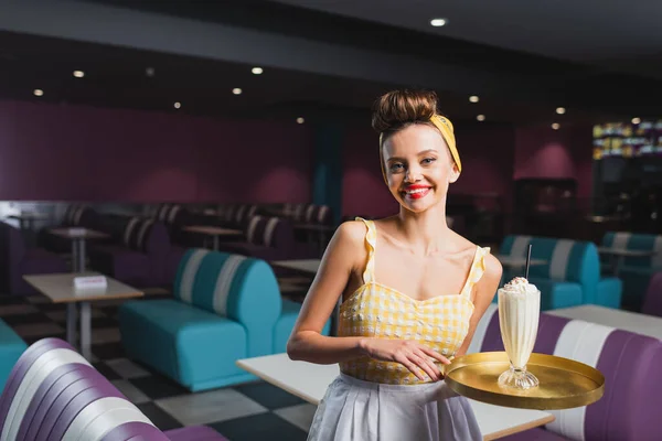 Alegre pin up camarera celebración bandeja con batido en la cafetería — Stock Photo