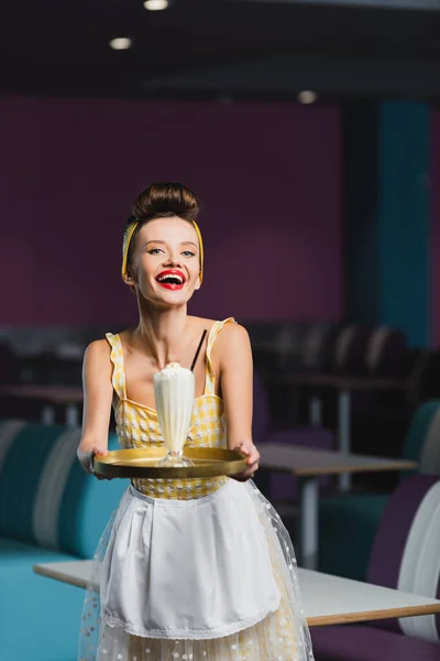 Amazed young pin up waitress holding tray with milkshake in cafe — Stock Photo